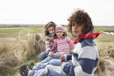 Children Sitting Amongst Dunes On Winter Beach