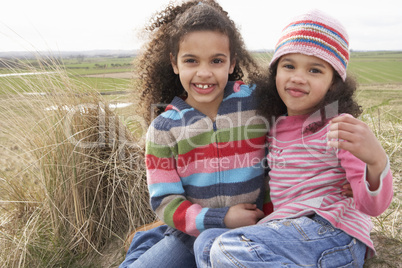 Young Girls Sitting Amongst Dunes On Winter Beach