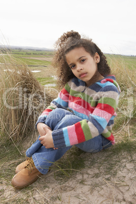 Young Girl Sitting Amongst Dunes On Winter Beach