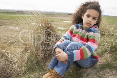 Young Girl Sitting Amongst Dunes On Winter Beach