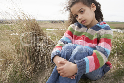 Young Girl Sitting Amongst Dunes On Winter Beach