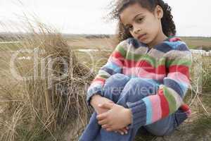 Young Girl Sitting Amongst Dunes On Winter Beach