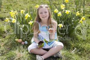 Girl Eating Chocolate Egg On Easter Egg Hunt In Daffodil Field
