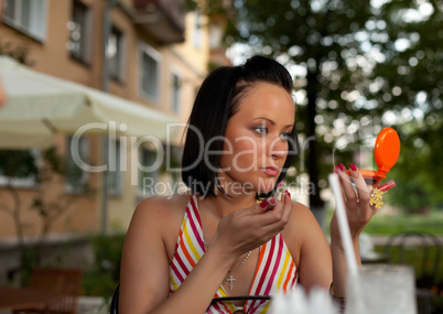 young woman in summer cafe applying cosmetics