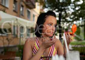 young woman in summer cafe applying cosmetics