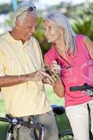 Happy Senior Couple Cycling Using Smart Phone Outside in Sunshin