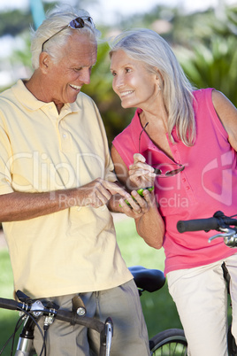 Happy Senior Couple Cycling Using Smart Phone Outside in Sunshin