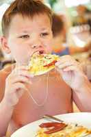 boy eats a pizza in summer cafe on a beach