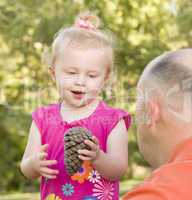 Young Girl Holding Pinecone with Her Dad in Park