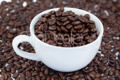 Small angled white cup of coffee with coffee beans