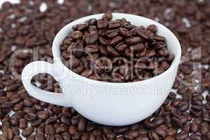 Small angled white cup of coffee with coffee beans