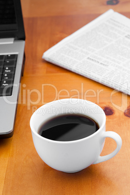 White cup of coffee with laptop and newspaper