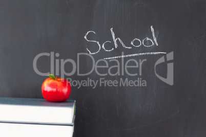 Stack of books with a red apple and a blackboard with "school" w