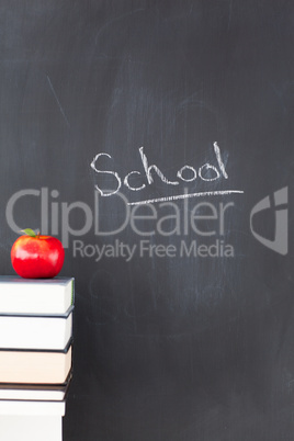Stack of books with a red apple and a blackboard with "school" w
