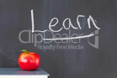 Stack of books with a red apple and a blackboard with "learn" wr