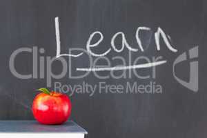 Stack of books with a red apple and a blackboard with "learn" wr