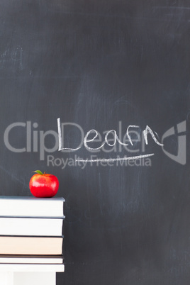 Stack of books with a red apple and a blackboard with "learn" wr
