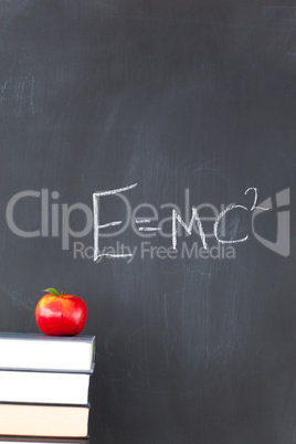 Stack of books with a red apple and a blackboard with a formula