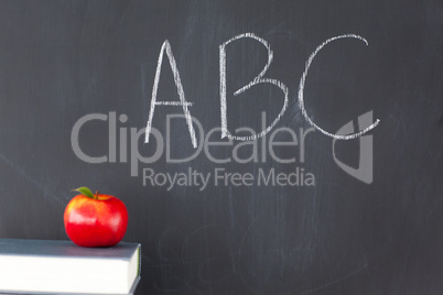 Stack of books with a red apple and a blackboard with "ABC" writ