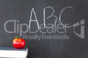 Stack of books with a red apple and a blackboard with "ABC" writ