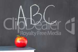 Stack of books with a red apple and a blackboard with "ABC" writ