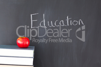 Stack of books with a red apple and a blackboard with "education