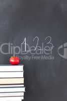 Stack of books with a red apple and a blackboard with "123" writ