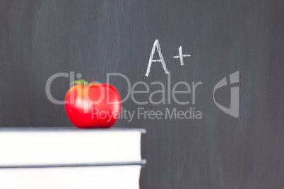 Stack of books with a red apple and a  blackboard with "A+" writ