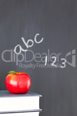 Stack of books with a red apple and a blackboard with figures an