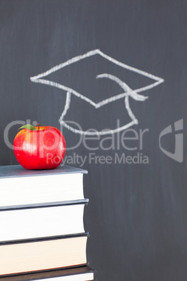 Stack of books with a red apple and a blackboard with a graduati