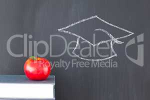 Stack of books with a red apple and a blackboard with a graduati