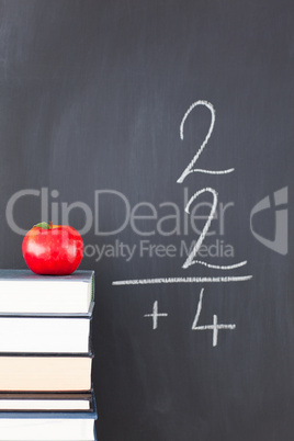 Stack of books with a red apple and a blackboard with a simple f