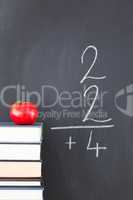 Stack of books with a red apple and a blackboard with a simple f