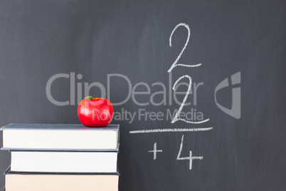 Stack of books with a red apple and a blackboard with a simple f
