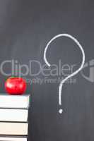 Stack of books with a red apple and a blackboard with "?" writte