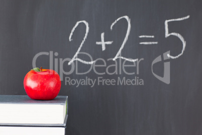 Stack of books with a red apple and a  blackboard with "2+2=5" w