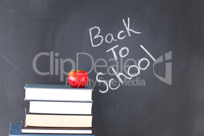 Stack of books with a red apple and a blackboard with "back to s