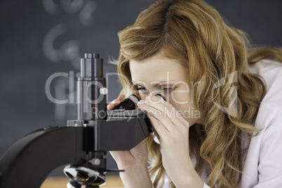 Blond-haired woman looking through a microscope