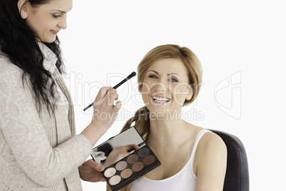 Attractive blond-haired woman having her make up done by a make