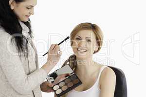 Attractive blond-haired woman having her make up done by a make