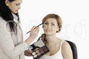 Cute blond-haired woman having her make up done by a make up art