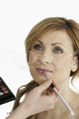 Young blond-haired female having her make up done by a make up a