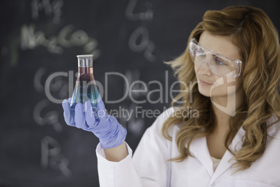 Young female scientist looking at a red and blue flask