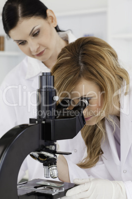 Cute scientist looking through a microscope with her assistant