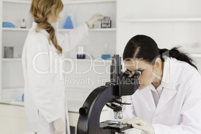 Dark-haired scientist looking through a microscope with her assi