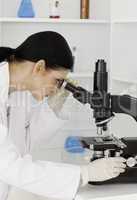 Dark-haired female looking through a microscope