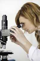 Cute blond-haired scientist looking through a microscope