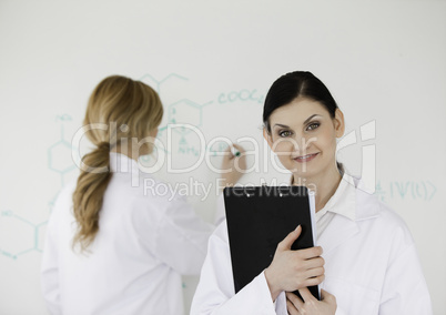 Scientist writting a formula helped by her assistant