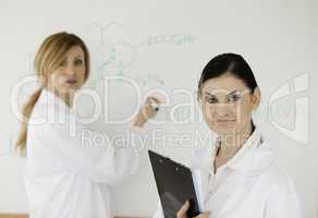 Cute scientist writting a formula helped by her assistant