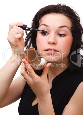 Woman is applying mascara while looking in mirror